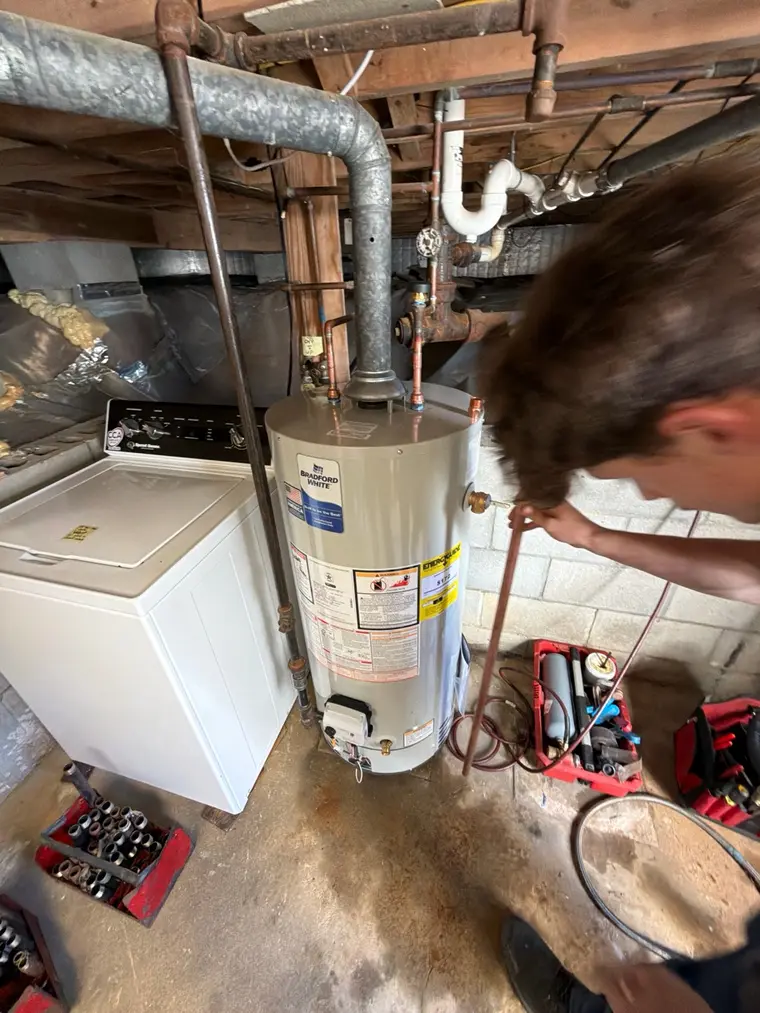 Technician working beside a Bradford White 40-gallon natural gas replacement water heater in a Dennis, MA basement
