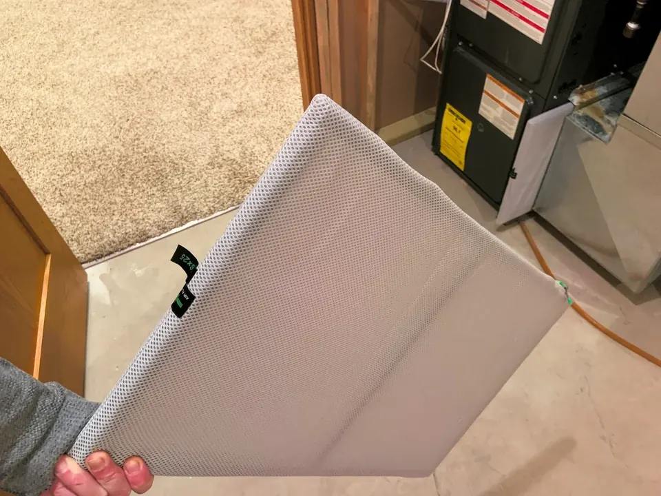 Reusable HVAC air filter being held beside a residential furnace