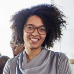 Smiling woman with glasses and curly hair, representing customer satisfaction and trust for Durfee Plumbing & Heating LLC's testimonials.