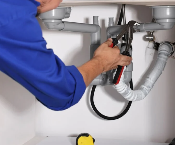 Plumber repairing under-sink plumbing with adjustable wrench, showcasing Durfee Plumbing & Heating's service expertise in plumbing solutions.